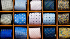 Cravatte eleganti uomo: espositore a scomparti con cravatte a fantasia azzurra, blu e ocra per abiti da cerimonia.