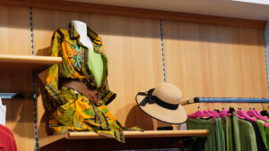 Allestimento reparto curvy Rovigo: manichino con abito estivo e cappello di paglia su ripiani in legno.