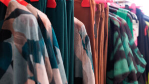 Abiti taglie comode donna: espositore con vestiti e maglie estive in tonalità verde e marrone.