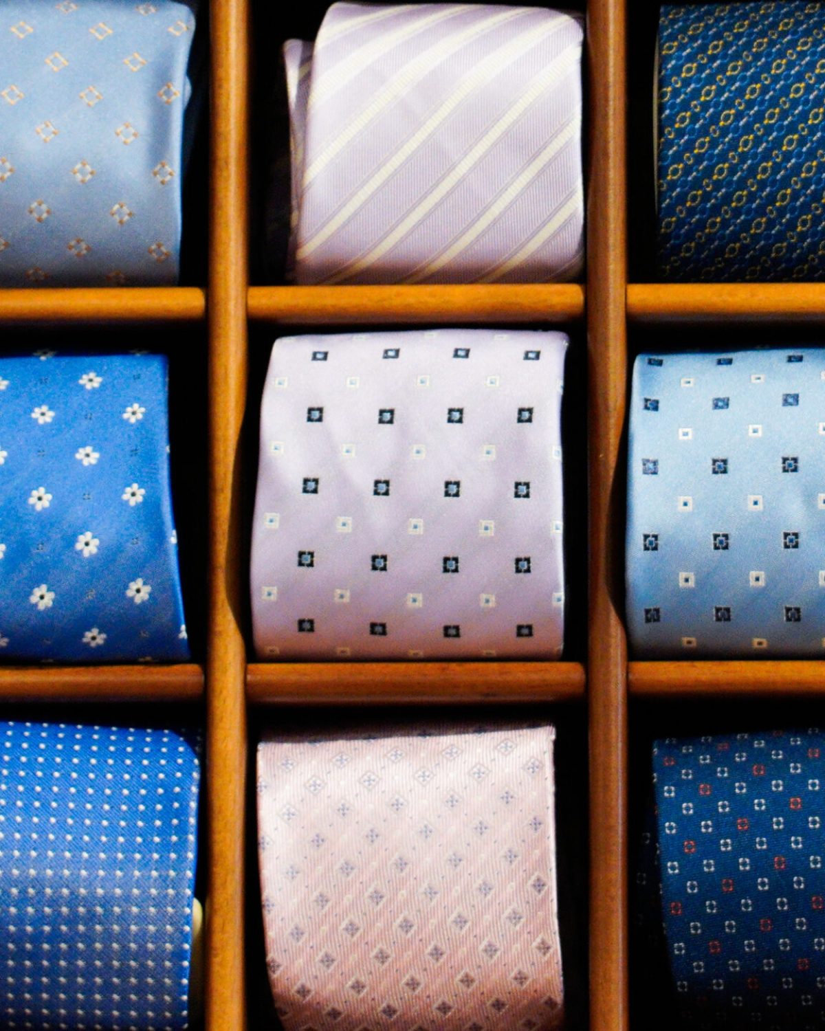 Cravatte eleganti uomo: espositore a scomparti con cravatte a fantasia azzurra, blu e ocra per abiti da cerimonia.