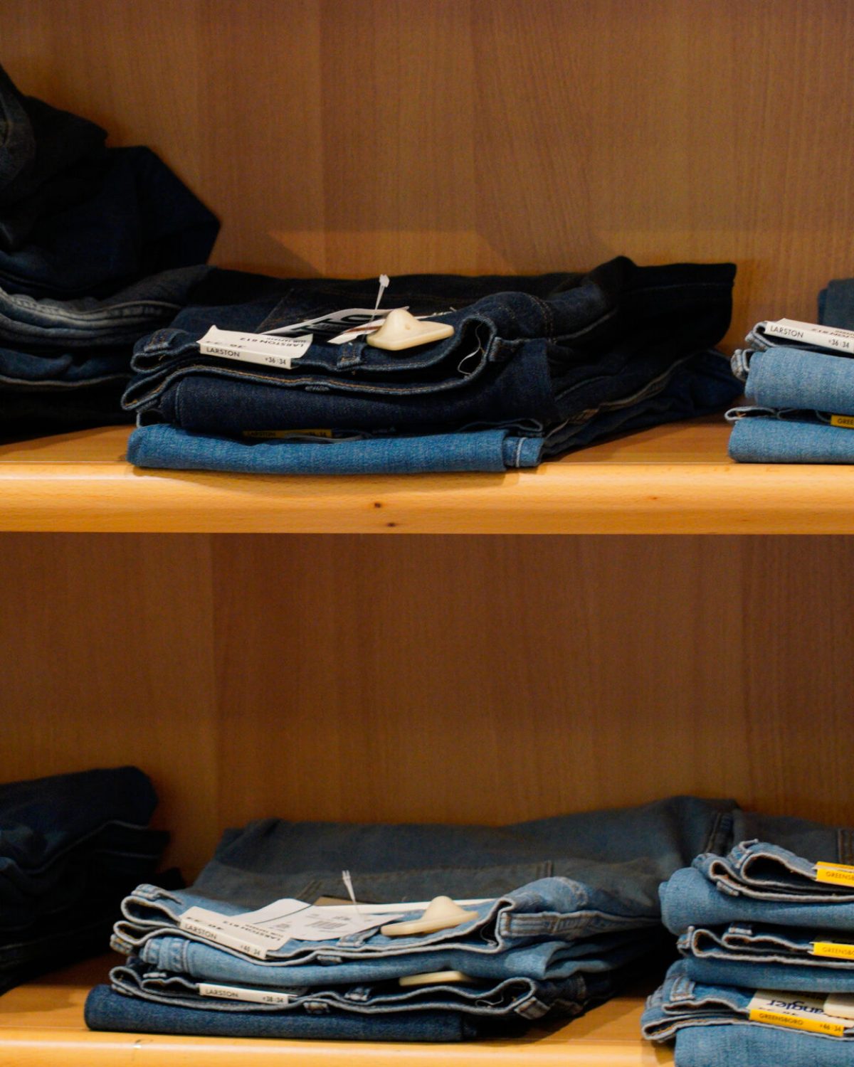 Jeans uomo taglie forti: espositore con pantaloni in denim Wrangler piegati su ripiani in legno.