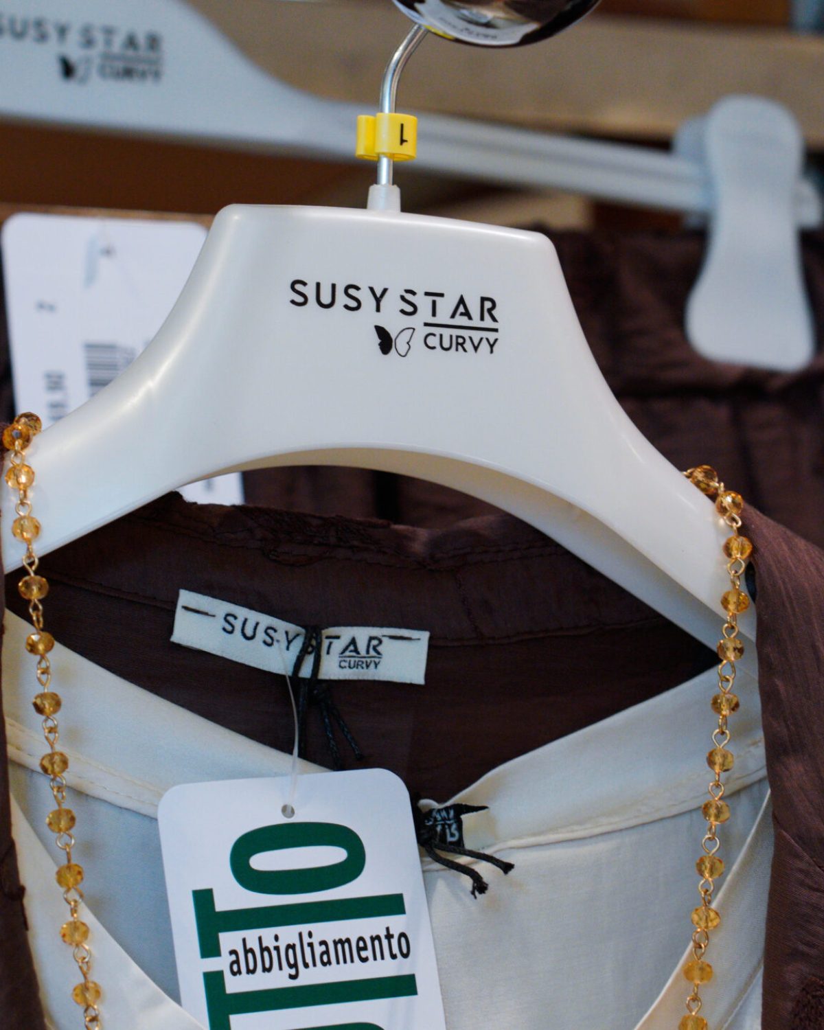 Accessori e abbigliamento curvy donna: dettaglio di collana su blusa marrone in espositore.