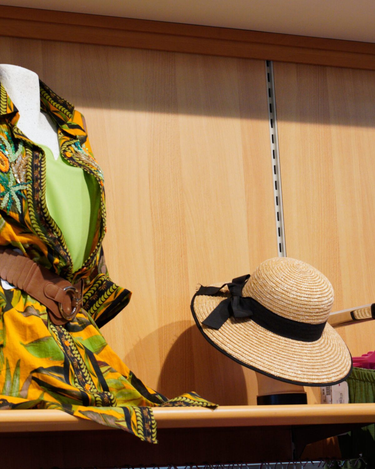 Allestimento reparto curvy Rovigo: manichino con abito estivo e cappello di paglia su ripiani in legno.