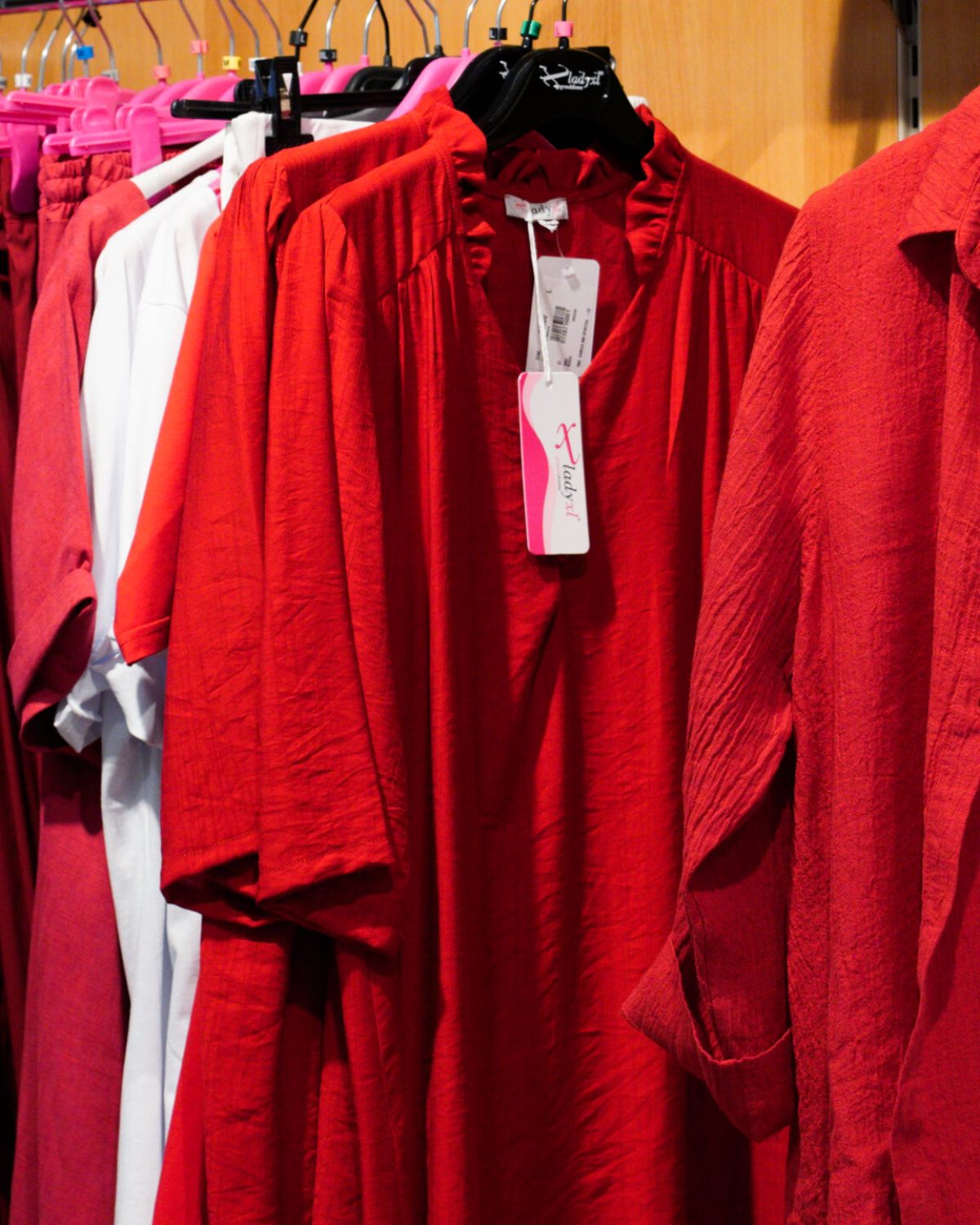 Abiti estivi taglie forti colorati: espositore con capi in rosso acceso e maglie con stampe.