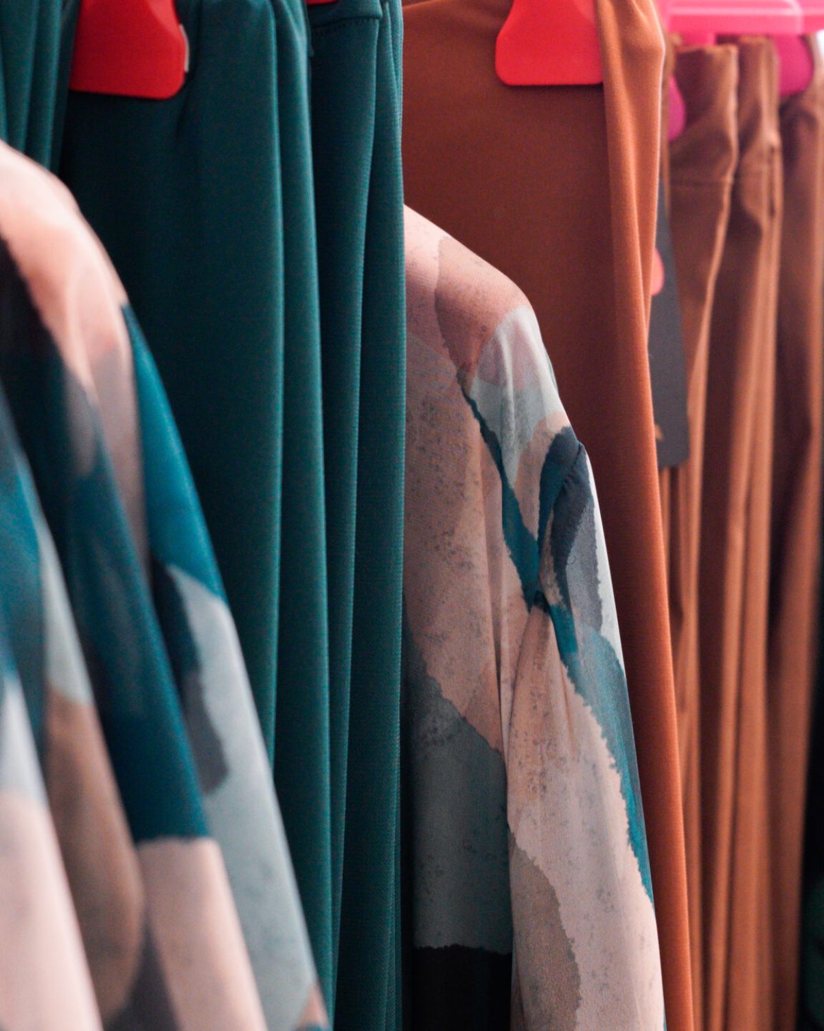Abiti taglie comode donna: espositore con vestiti e maglie estive in tonalità verde e marrone.